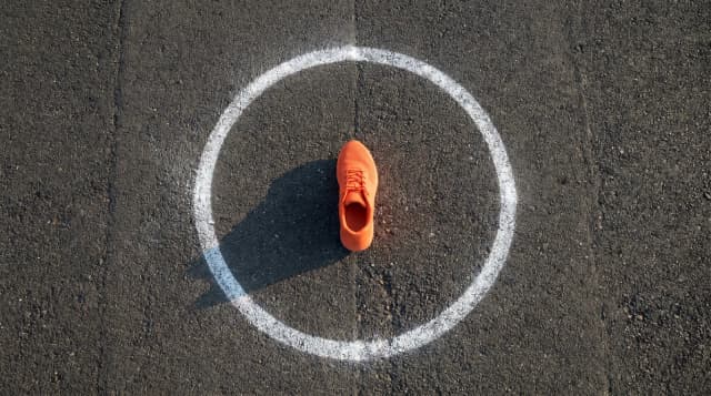 Chaussure de sport orange au centre d'un cercle de craie sur piste noire