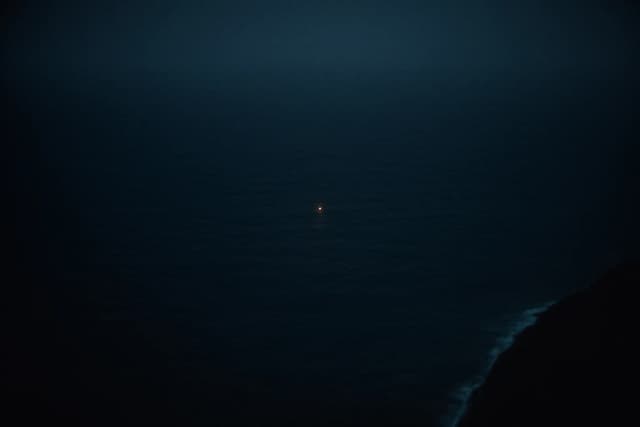 Vue satellite sombre d'un océan de nuit presque entièrement noir, un unique minuscule point lumineux brillant très au large là où rien d'autre n'est visible, un trait de côte à peine perceptible sur le bord
