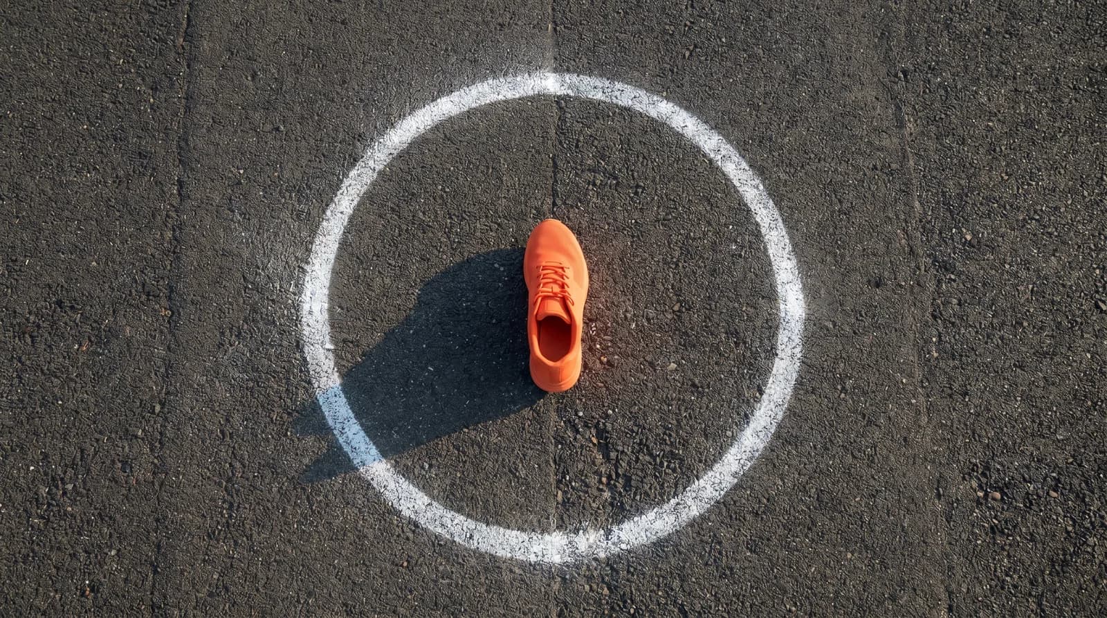 Chaussure de sport orange au centre d'un cercle de craie sur piste noire, métaphore visuelle de l'orbite du nouveau logo Décathlon