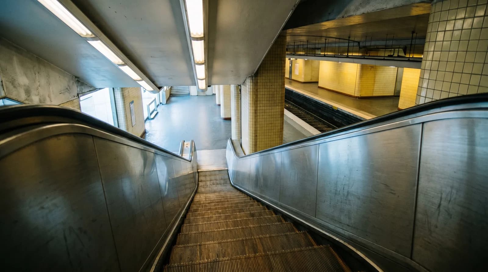 Escalator de métro parisien descendant vers un quai vide à l'aube, métaphore visuelle de la mobilité publique modernisée silencieusement