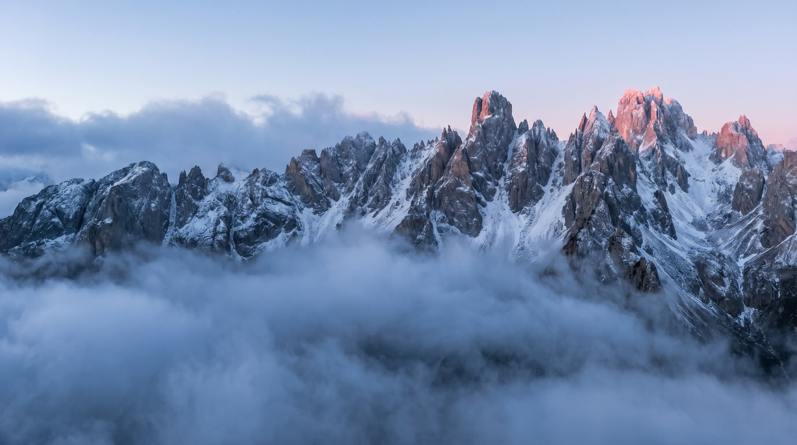 Crête de montagne déchiquetée au-dessus de nuages bas à l'aube, sans aucune construction humaine, métaphore visuelle de la marque transmise à la Terre