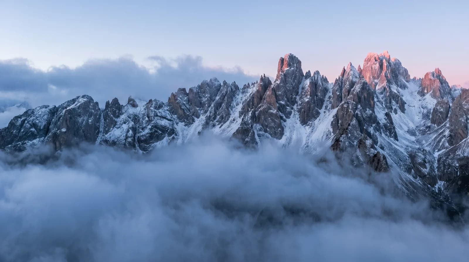 Crête de montagne déchiquetée au-dessus de nuages bas à l'aube, sans aucune construction humaine, métaphore visuelle de la marque transmise à la Terre