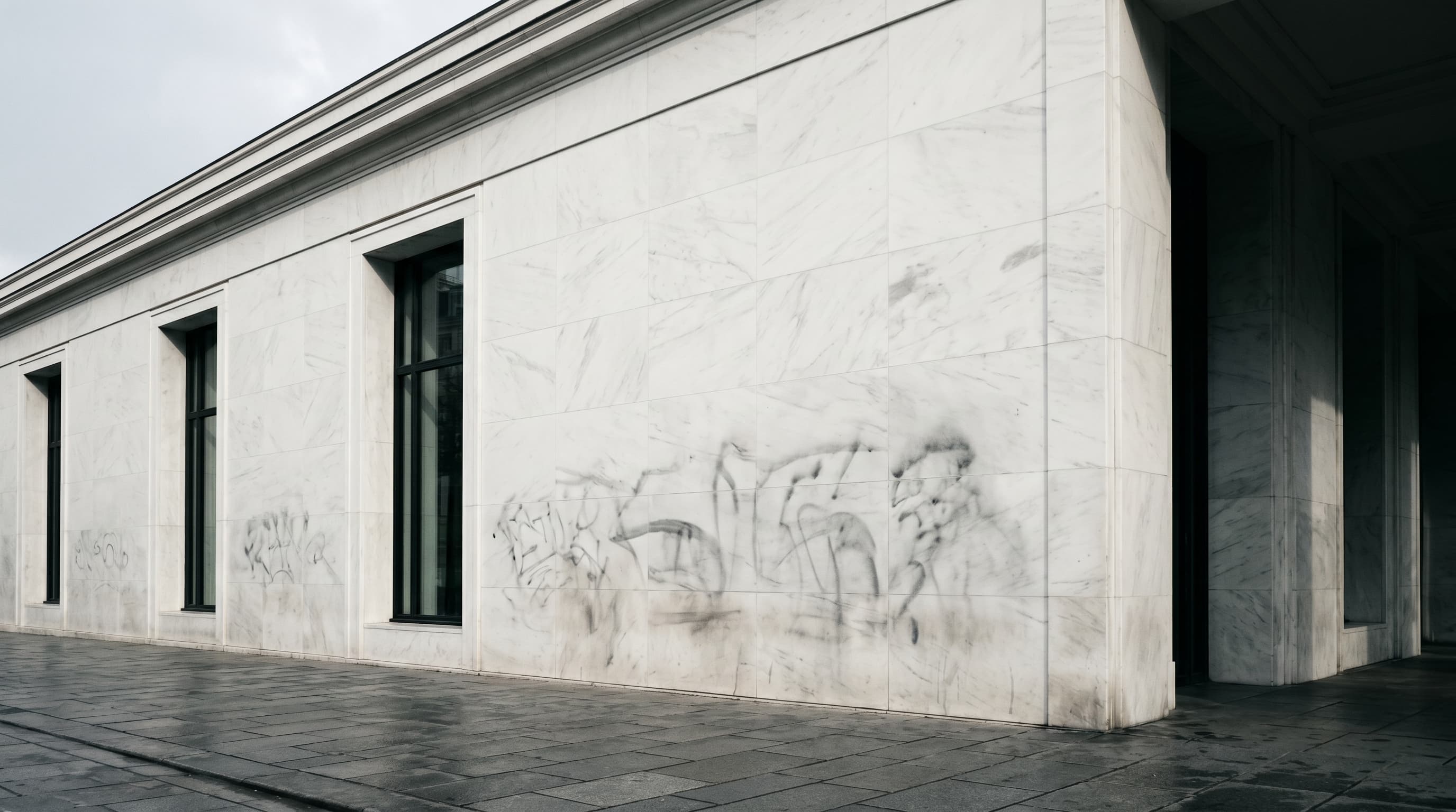Façade de marbre blanc immaculée laissant deviner les traces sombres d'un graffiti effacé en dessous, métaphore visuelle du rebrand cohérent qui n'a pas traité les passifs