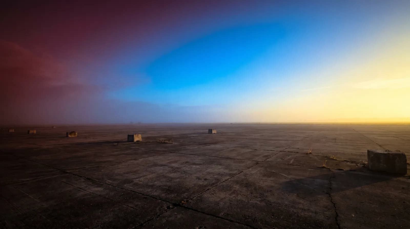 Horizon vide avec ciel en gradient rouge-bleu-jaune sur sol industriel, métaphore visuelle du passage du pétrole aux énergies multiples