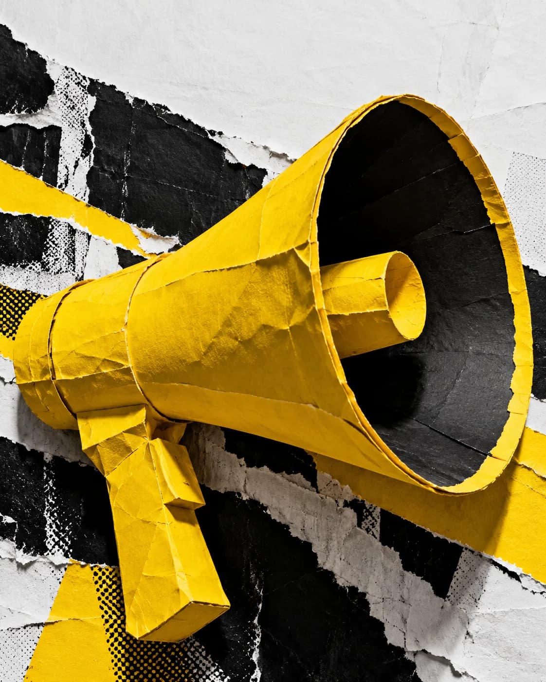 Mégaphone jaune sculpté en papier, sur un collage d’affiches déchirées noires et blanches