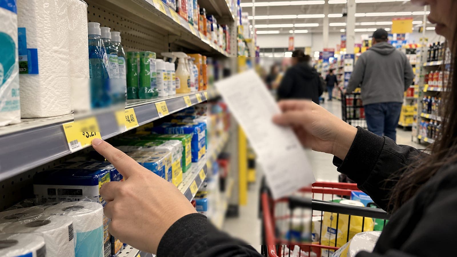 Dans un rayon de supermarché, une cliente pointe une étiquette de prix et tient son ticket de caisse